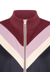 Rundhalsad jacka med dragkedja som har maroon, rosa, krämfärgade och marinblå zigzag-mönster, texturerat tyg och en gyllene dragkedja.