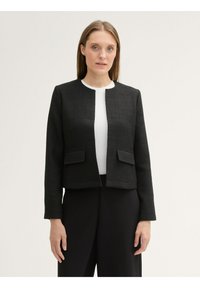 Chaqueta negra texturizada con cuello redondo, bolsillos delanteros y mangas largas, combinada con una blusa blanca y pantalones negros.