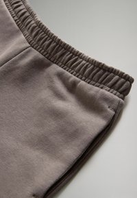 Pelēki sporta bikses ar mīkstu tekstūru, ar elastīgu jostu un gludu apdari, attēlotas no slīpa sānu skata.