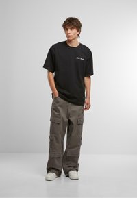 Black cotton t-shirt with short sleeves, paired with gray cargo pants featuring multiple pockets and a loose fit; white sneakers.