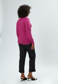 Maglione fucsia a maglia con maniche lunghe abbinato a pantaloni neri con risvolto e décolleté neri con perle decorative.