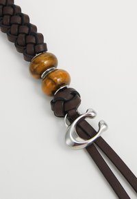 Brown braided leather strap featuring two glossy orange beads and a silver metal hook clasp. Smooth texture with shiny accents.