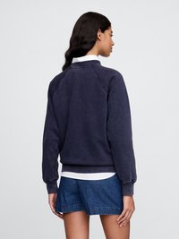 Granatowa bluza z raglanowymi rękawami i ściągaczem na dole, o miękkiej teksturze, założona na białą koszulę z kołnierzykiem.