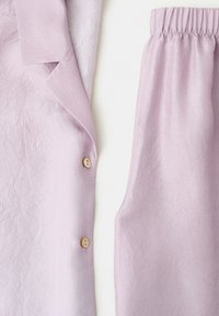 Halenková košeľa z fialovo-lila zmraštenej látky s gombíkmi na ľavej strane a nohavice s elastickým pásom na pravej strane, uložené na bielom podklade.