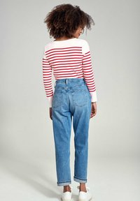 Top à manches longues rouge et blanc à rayures, associé à un jean en denim bleu taille haute avec des poignets retroussés et des baskets blanches, vu de l'arrière.