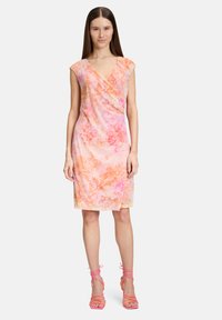 Robe tie-dye rose et orange avec un design croisé, de courtes manches à encolure, et une longueur au genou, accompagnée de talons roses à lanières.