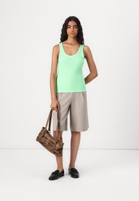 Light green tank top with a scoop neck, paired with light gray shorts. Brown textured handbag, black slip-on shoes, and neutral background.