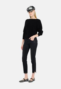 Maglione nero a maglia, jeans neri slim-fit con spacchi laterali e ballerine grigie a fantasia. Berretto nero e grigio con dettagli. Texture morbide.