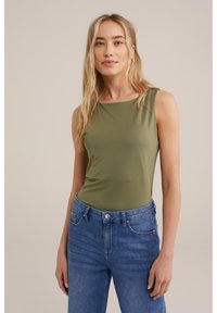 Olivno zeleni top brez rokavov iz gladkega, prilagodljivega materiala, v kombinaciji z modrimi jeans hlačami visoko pasu, ki se ponašajo s klasično teksturo denima in vidnimi šivi.