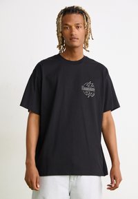 Camiseta de algodón negra con mangas cortas, escote redondo y un gráfico de logo en el frente con rayos. Corte relajado.