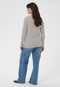 Langærmet, stribet top i creme og brun, parret med lyseblå vidde jeans og sorte flade sko. Casual fit og afslappet design.