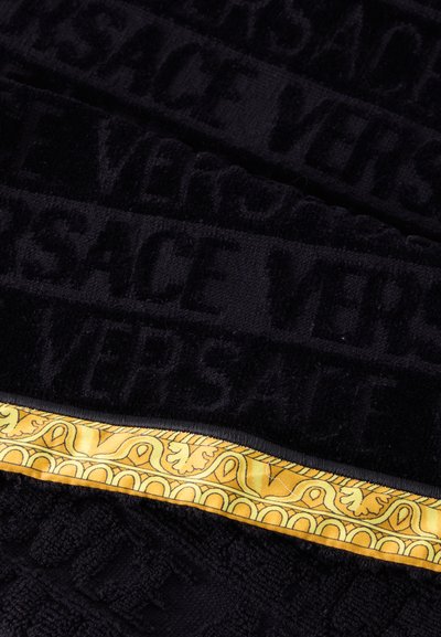 Tissu noir texturé avec le texte "VERSACE" répété et une bordure décorative jaune présentant des motifs ornés.