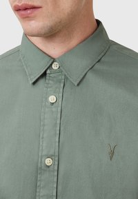 Lichtgroene shirt met een button-down kraag, lichtgekleurde knopen en subtiele geborduurde details van een horned dier op de borst.