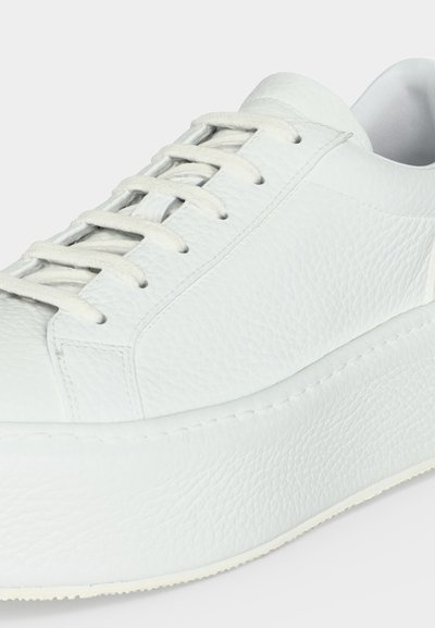 Baskets blanches en cuir avec surface texturée, semelle épaisse et lacets blancs, vues en gros plan de côté.