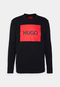 Černá mikina s velkým červeným obdélníkovým panelem, na kterém je vytištěný nápis "HUGO" tučnými černými písmeny. Měkká tkanina, kulatý výstřih, dlouhé rukávy.