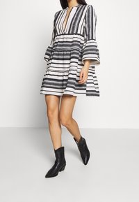 Robe à rayures noires et blanches avec un col en V, des manches évasées et une jupe à volants. Portée avec des bottes de cowboy noires. Tissu à texture lisse.