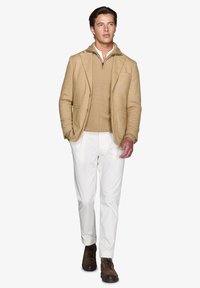 Beige blazer med tekstureret væv, lagdelt over en tan striktrøje, parret med hvide bukser og brune snørebåndsstøvler.
