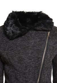 Chaqueta de mezcla de lana negra y gris que presenta una capucha de piel sintética, cierre de cremallera asimétrico y tejido texturizado.