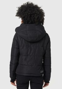 Doudoune noire avec capuche, présentant des sections matelassées, des poignets élastiques et une étiquette de marque en bas. Texture douce et lisse.
