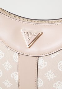 Sac à main en simili cuir beige avec un logo doré en forme de triangle, fermeture zippée et motif en relief comportant des symboles stylisés sur la surface.