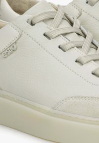 Bílé kožené tenisky s texturovanými akcenty, kulatou špičkou, minimalistickým designem, plochými šňůrkami a subtilním logem na boku. Měkká vnitřní podšívka.