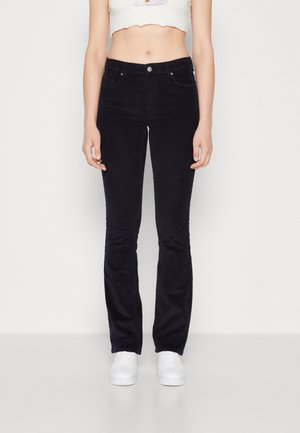 Navy corduroy flared jeans with two front pockets and a single metal button closure. Worn with a cropped white top and white sneakers.