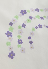 Vitt tyg med ett mönster av lila och gröna blommor i en regnbågsform, med små guldaccent i blommitten.