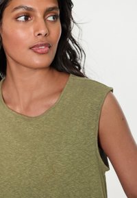 Grøn ærmeløs top med rund halsudskæring, lavet af en blød, tekstureret stof med en lys, plettet finish og subtile pletdetaljer.