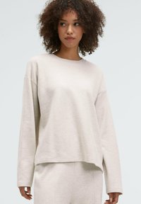 Light beige, oversized sweatshirt with long sleeves, crew neck, and soft texture. Paired with matching pants for a cohesive look.