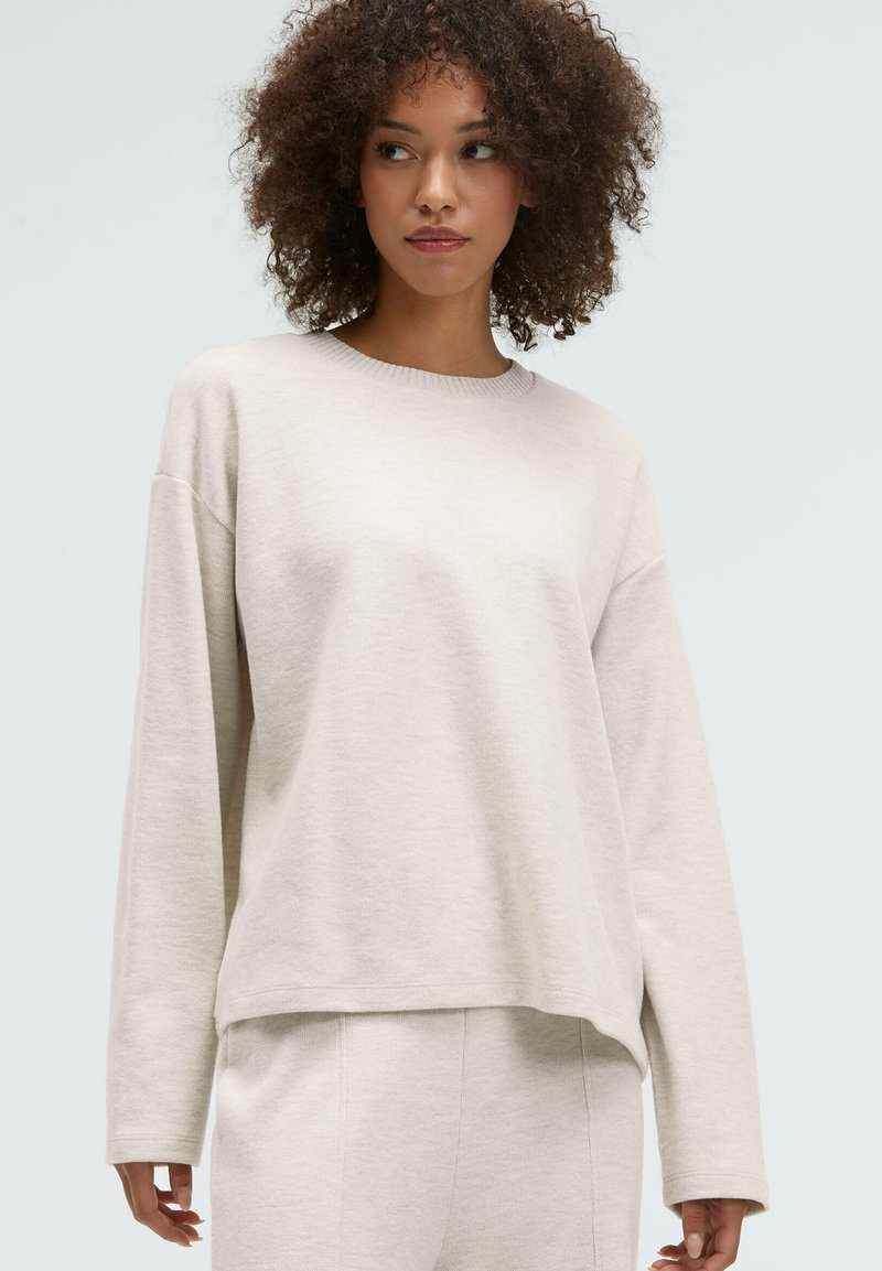 Light beige, oversized sweatshirt with long sleeves, crew neck, and soft texture. Paired with matching pants for a cohesive look.