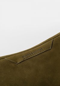 Olivenfarbene Wildledertasche mit glatter Textur, ausgestattet mit geprägtem Markenlogo und dezenten Nähten entlang der oberen Kante.