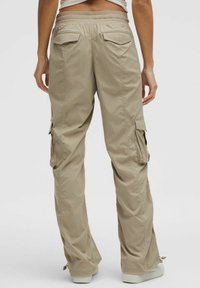 Beżowe spodnie cargo z teksturowanym wykończeniem, z dwoma tylnymi kieszeniami i bocznymi kieszeniami cargo. Elastyczny pasek w talii i zwężane mankiety.