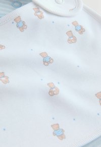 Heleheline bib, millel on pehme tekstuur ja korduv muster väikestest karudest triibulistes särkides ning laiali hajutatud sinistest tähtedest.