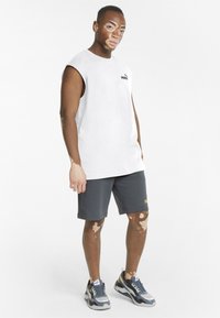 Hvid ærmeløs skjorte, grå shorts med logo og grå sportssko med gule detaljer. Glat tekstur og afslappet design.