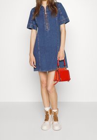 Jeansklänning med korta ärmar, med dragkedja framtill och en strukturerad snitt. Kombinerad med en liten röd handväska och beige stövlar med vita snören.