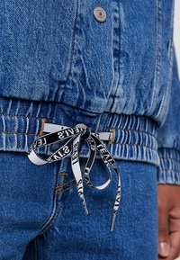 Blue denim jacket with elastic waistband tied with black and white drawstring labeled "Levi's," worn over matching blue jeans.