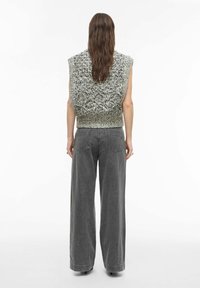 Stickad väst i svart och vitt med bred axeldesign, kombinerad med högmidjade grå vida jeans med bakfickor och lös passform.