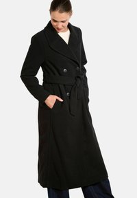 Czarny płaszcz trench z podwójnym zapięciem, dużymi klapami, paskiem do związywania i bocznymi kieszeniami; wykonany z miękkiej, teksturowanej tkaniny.