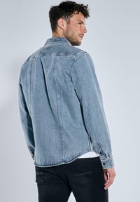 Hellblaues Jeansjackett mit spitzem Kragen, langen Ärmeln und abgerundetem Saum. Verfügt über einen Schulterbereich und knöpfbare Manschetten.