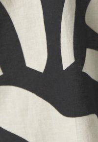 Motif abstrait noir et crème sur tissu, mettant en valeur des formes courbes et un matériau léger et texturé.