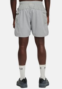 Ljust grå träningsshorts har en elastisk midja, två sidofickor och en slät yta. Bärs med grå skor och vita strumpor.