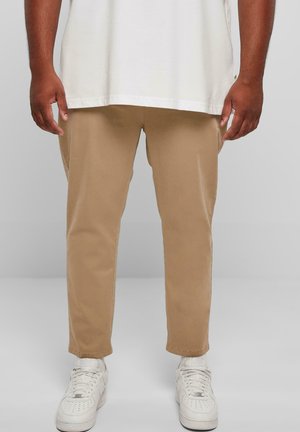 Chino khaki cu picioare drepte, din material de bumbac, cu buzunare laterale vizibile, asortați cu adidași albi și un tricou alb, lejer.