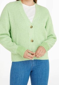 Hellgrüner gerippter Cardigan mit V-Ausschnitt, ausgestattet mit zwei großen braunen Knöpfen und langen Ärmeln. Das strukturierte Strickmaterial verleiht dem Stück Dimension.