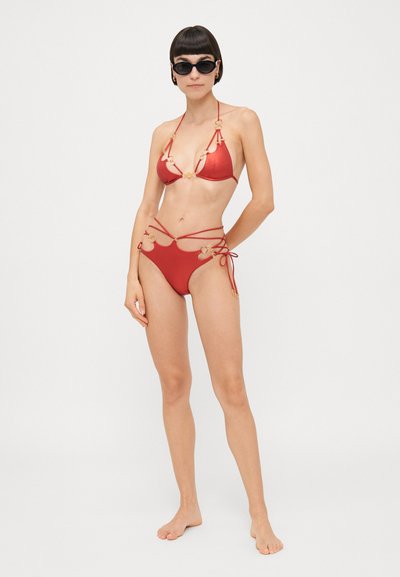 Red bikini set made of smooth material, featuring gold hardware accents, triangular top, and adjustable ties on the bottom.