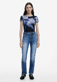 Kitsas tumesinine topp abstraktse kujundusega; helesinised sirged teksad punaste lilleline tikandiga külgedel; mustad kingad roheliste paeltega.