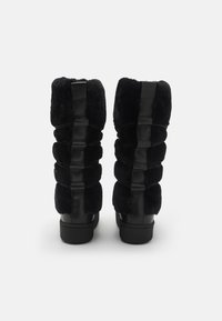 Svarta knähöga stövlar med mjukt tyg med ribbad design och glansiga läderdetaljer, rundad tå och flat sula.