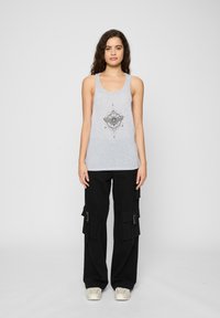 Graues Tanktop mit einem zentralen schwarzen grafischen Design, kombiniert mit schwarzen Cargo-Hosen mit großen Seitentaschen und einem lockeren Schnitt.