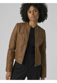 Giacca di pelle marrone con chiusura a zip, colletto rialzato e tasche sul petto diagonali. Texture liscia e vestibilità su misura, abbinata a un top nero.