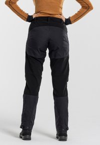 Zwarte en grijze broek met een gestructureerde pasvorm, voorzien van versterkte naden, verstelbare enkelboorden en een duurzame stof voor buitengebruik.