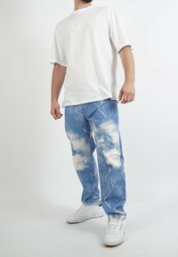 Camiseta blanca de algodón de manga corta, combinada con vaqueros azules de mezclilla con estampado de nubes y patrones de rayos. Zapatillas blancas.